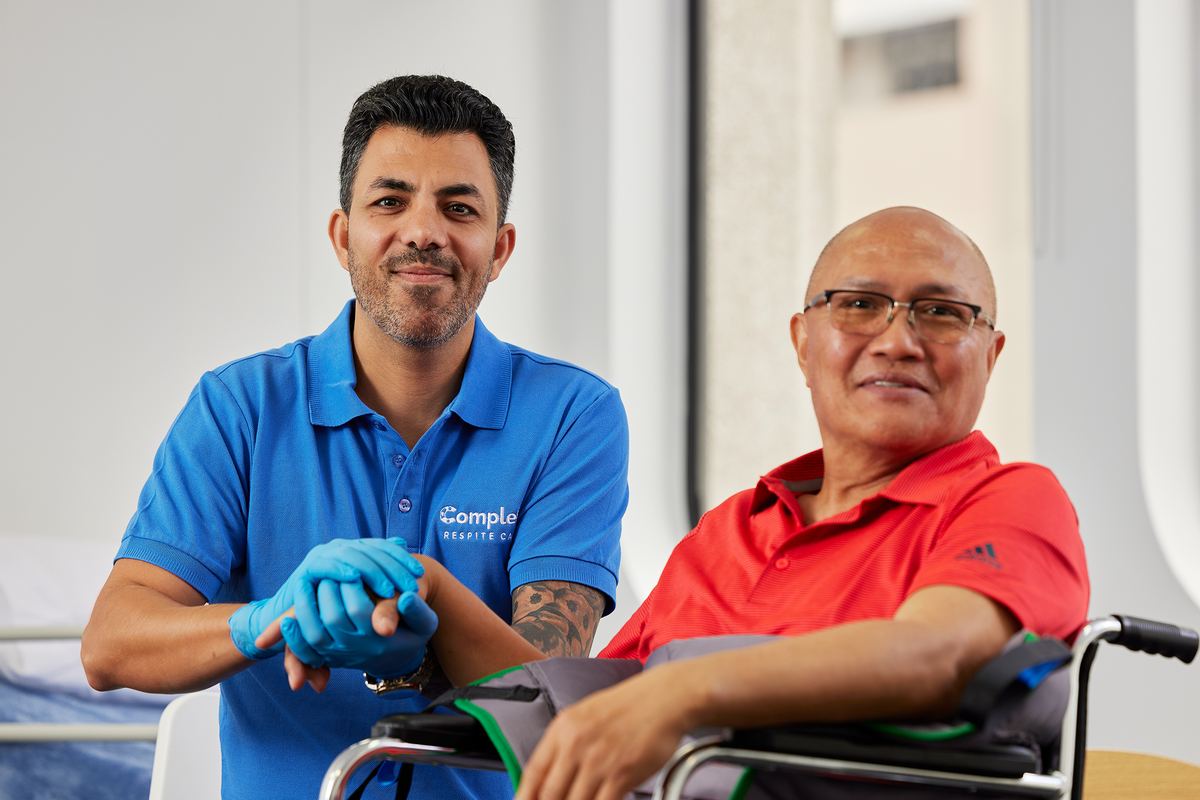 A carer gently holding the hand of an older client, both looking at the camera